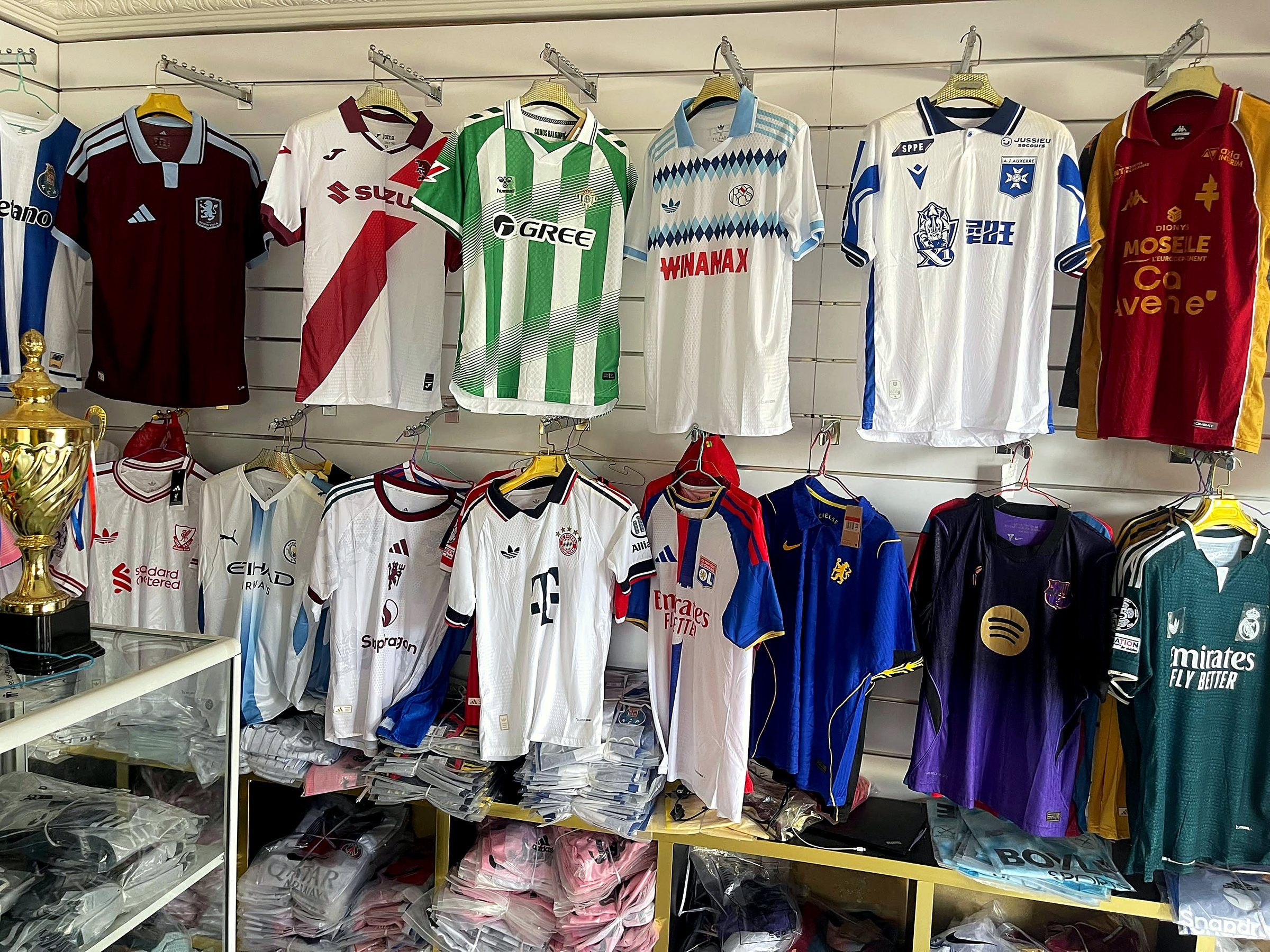 Mur de maillots de clubs suspendus dans la boutique Door Gainde, avec un trophée doré à gauche