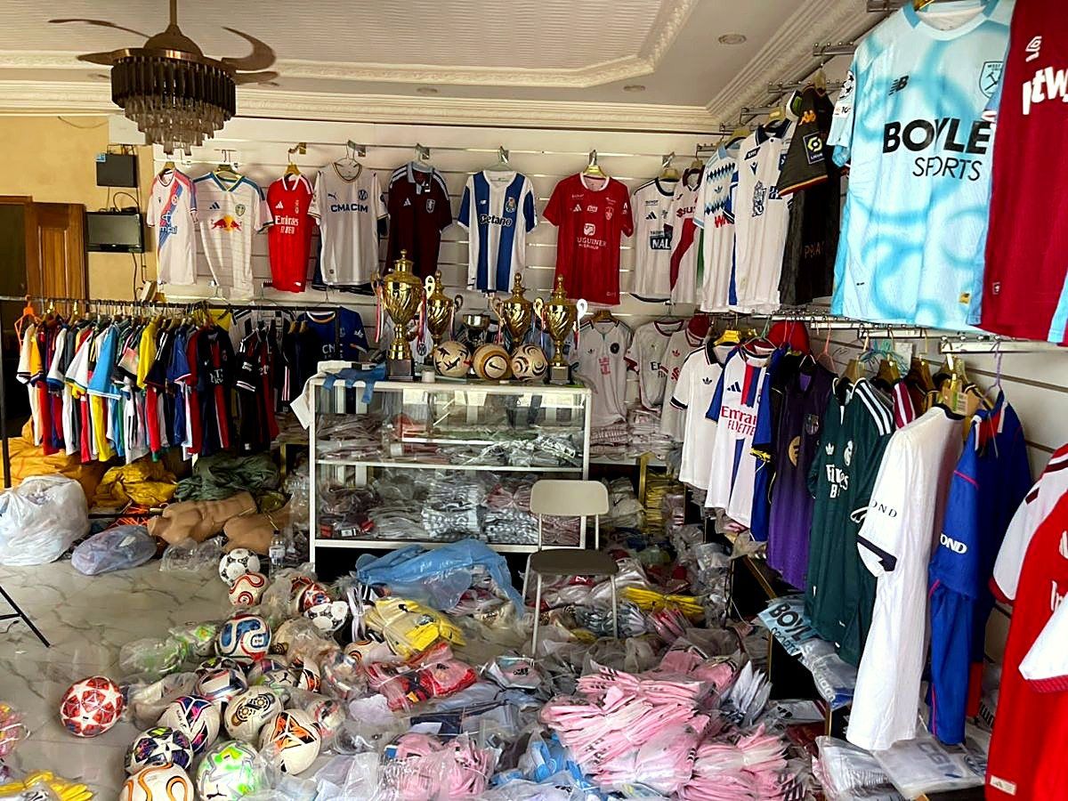 Intérieur de la boutique : maillots aux murs, trophées et ballons sur la vitrine, ballons au sol
